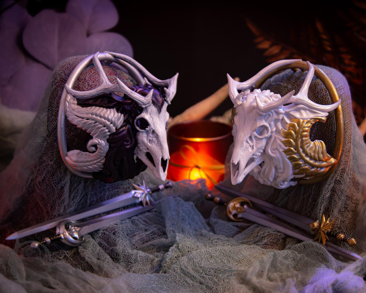 Two resin hair bun covers set up on stands, with their resin sword pins. The bun covers are antlered deer (stag) skulls with gilded ferns.